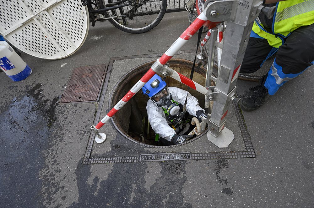 Un salarié descend équipé dans une bouche d'égout.